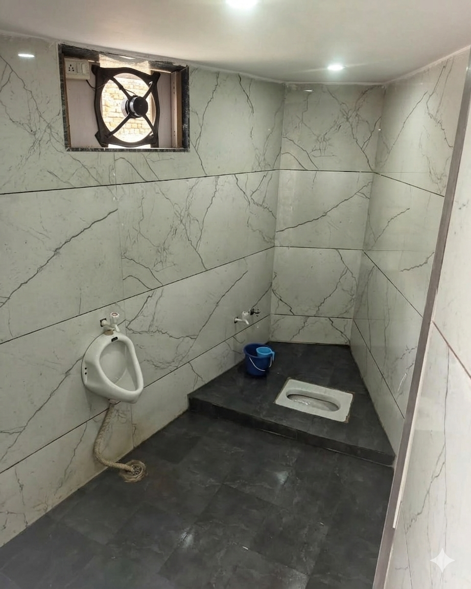 Clean and well-ventilated washroom facility at the library. Features an Indian-style toilet, separate urinal, premium wall tiles, and an exhaust fan for proper hygiene and odor control.